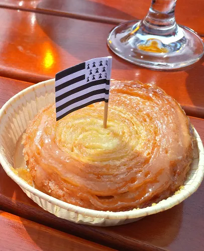 Kouign-amann breton glacé avec un drapeau breton miniature, sur une table en bois.