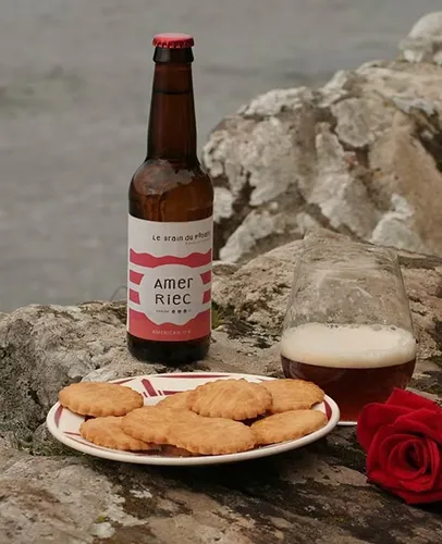 Bière, biscuits et rose rouge sur rochers face à l'eau.