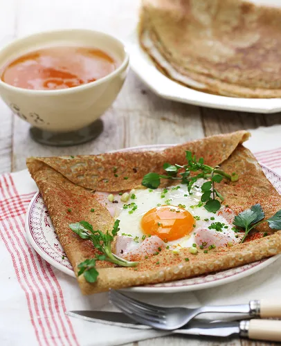 Crêpe salée garnie d'un œuf au plat, jambon, ciboulette, paprika, et persil.