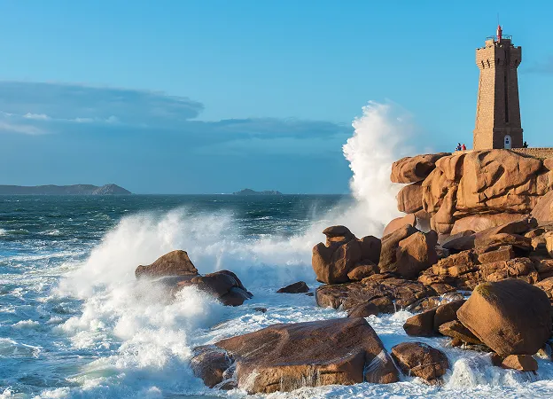 Phare rocheux au bord de la mer, grandes vagues déferlant sur les rochers.
